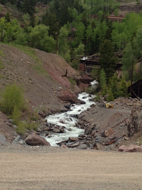 A creek flows down a rocky ravine, a small bridge crosses it