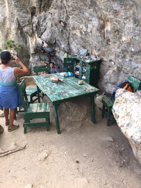 Green table, chairs and cabinet sitting on a rock slab backed by tall rock. Some people are taking pictures.