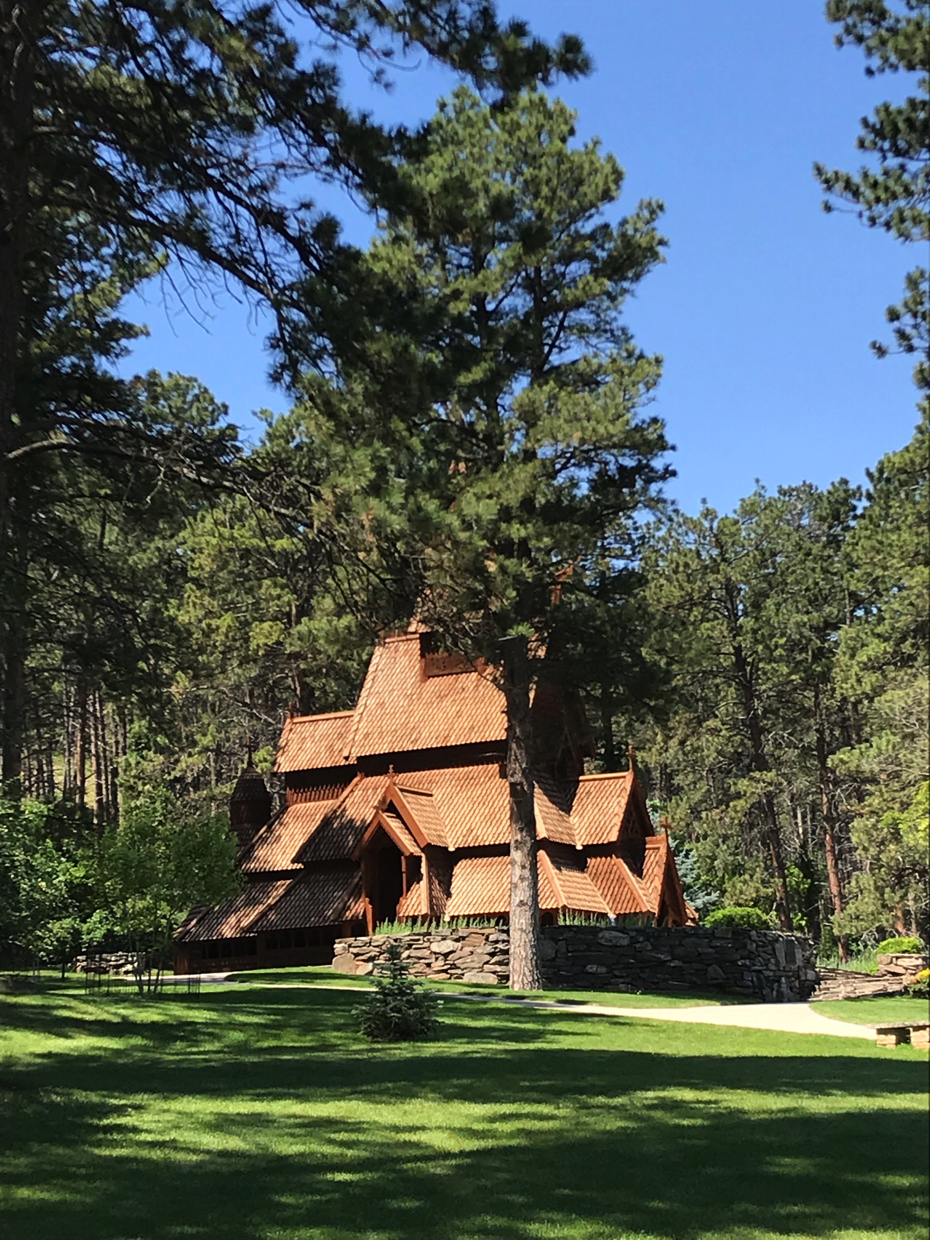 A wooden church stands amongst trees on a green lawn