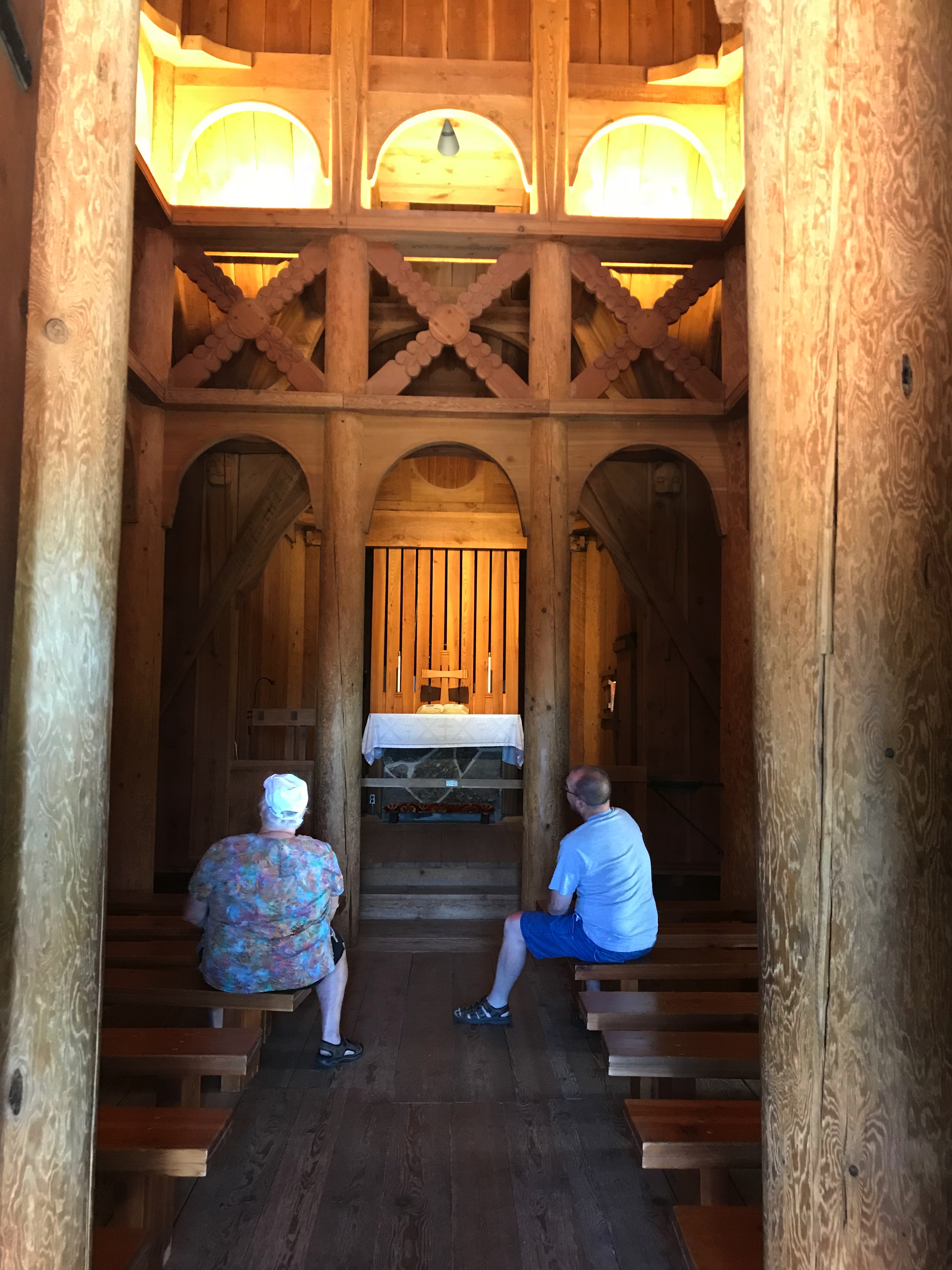 Rear view of two people, a man and a woman, sitting on wooden benches looking around the interior of a wooden church.