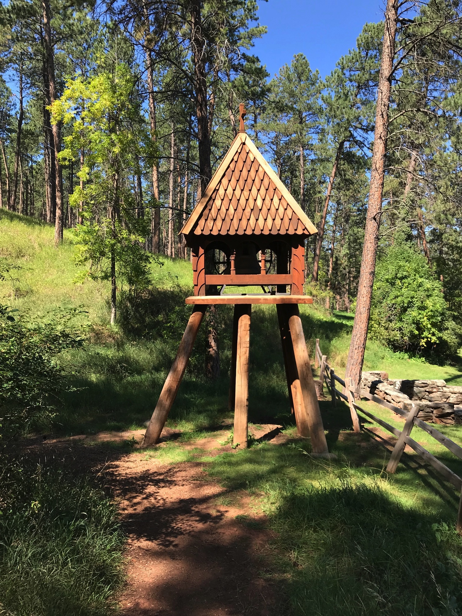 A wooden, bell tower sits on a dirt path in the woods