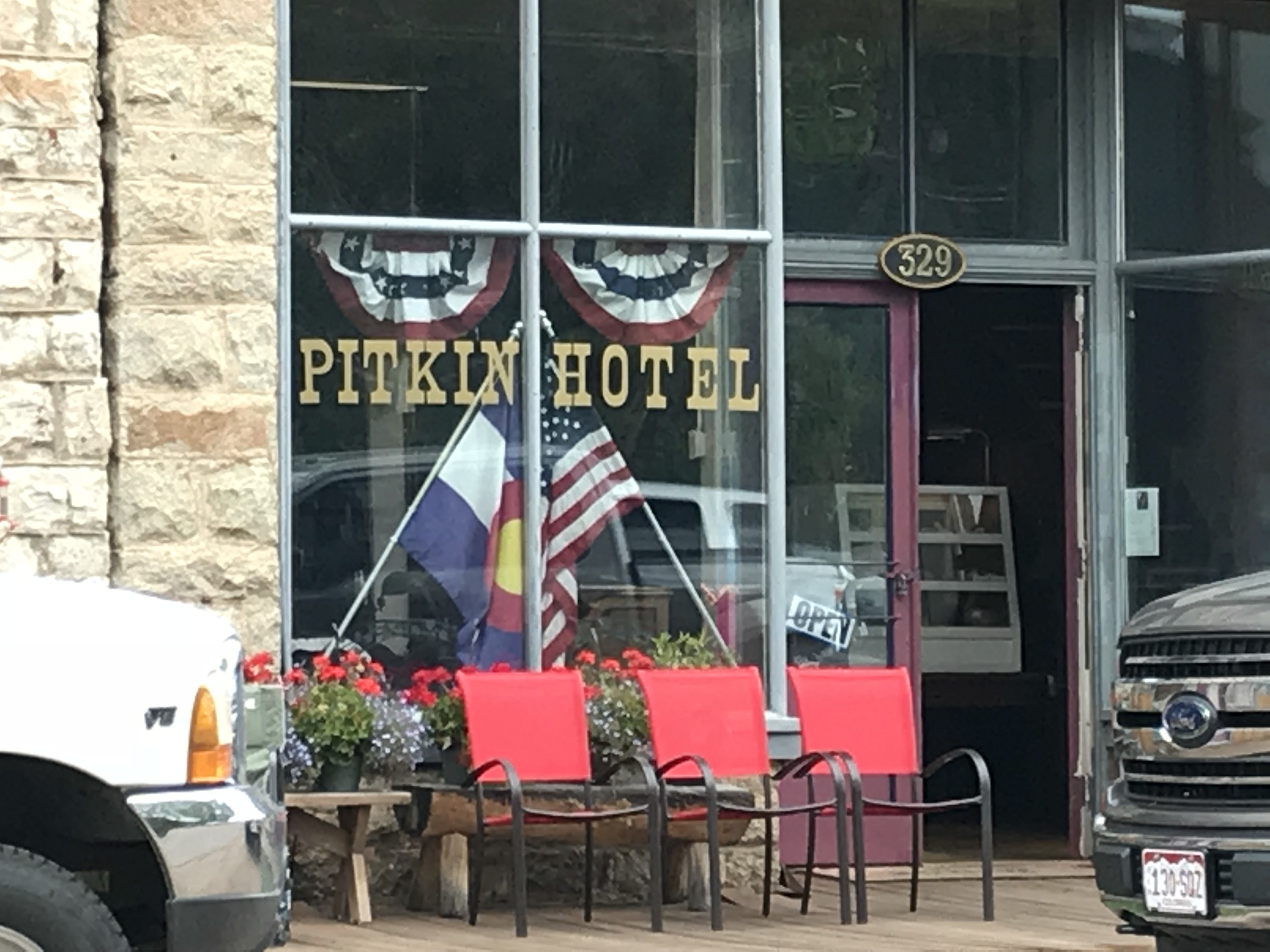 Letters read "Pitkin Hotel" on the glass front of the building. Modern-day trucks sit on the street out front
