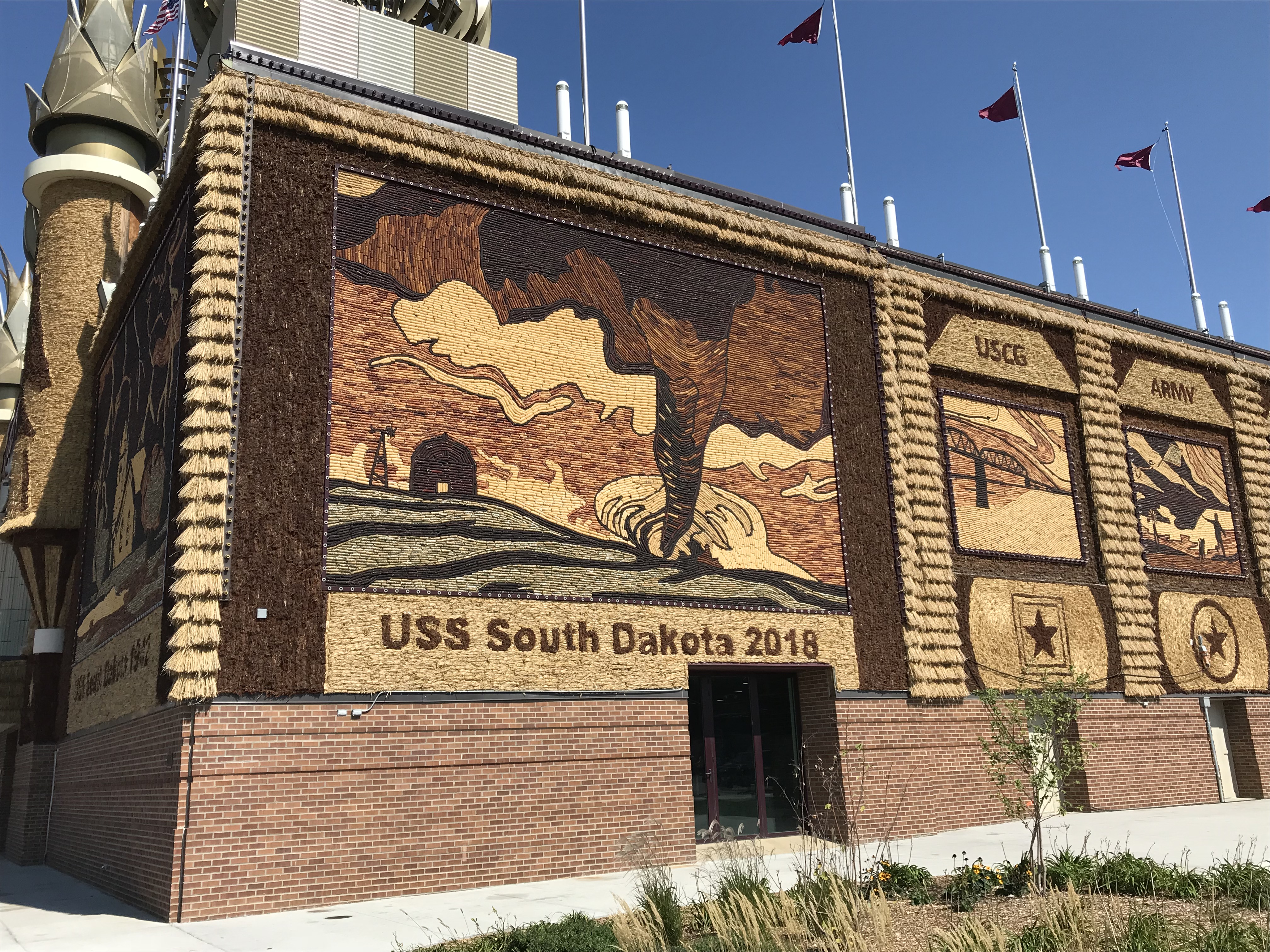 A building with a mural or a tornado running across a field towards a barn and the words, "USS South Dakota 2018" on it. 